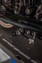 Load image into Gallery viewer, Close-up of chrome center stand mounting under a Harley-Davidson Softail